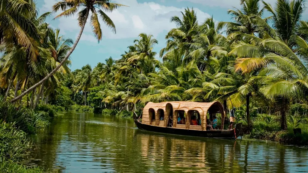 A serene scene of the backwaters in Kerala, with lush green palm trees lining the banks and traditional houseboats floating on the calm water.